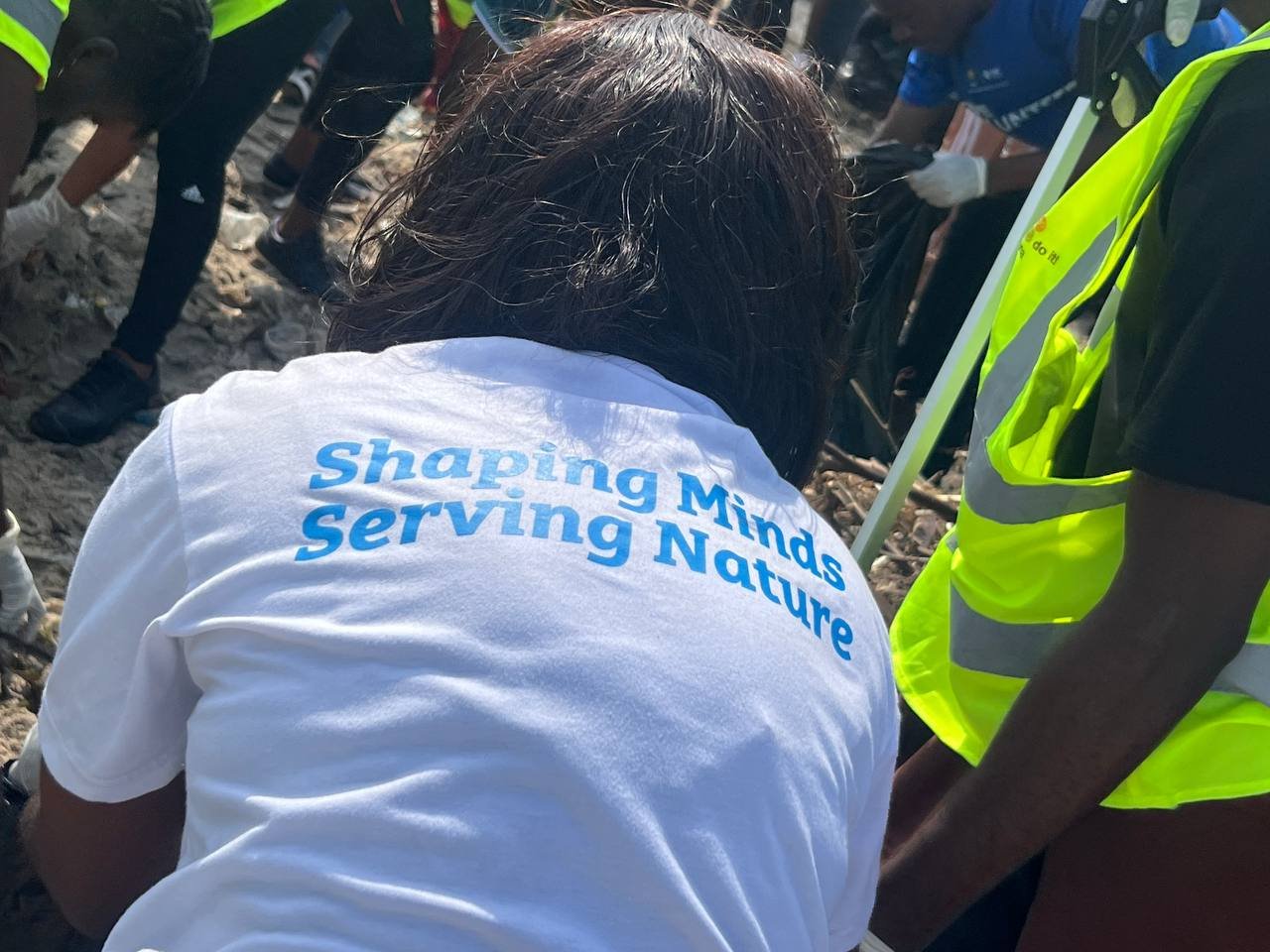 Volunteer in a "Shaping Minds, Serving Nature" t-shirt during a beach clean-up