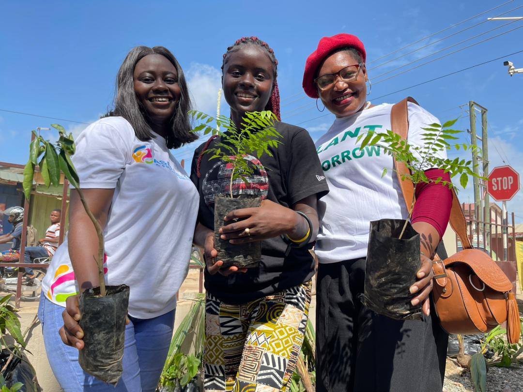 Three Asaase Yaa volunteers smiling and holding tree seedlings ready for planting